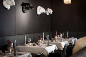 Lehrlingsportal.at Ein modernes Restaurant mit gedeckten Tischen; an den schwarzen Wänden befinden sich dekorative Schafskopfskulpturen in Schwarz und Weiß.