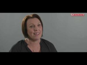 Lehrlingsportal.at Eine Frau mit kurzen braunen Haaren lächelt, während sie leicht aus der Kamera schaut; das Bauhaus-Logo erscheint in der oberen rechten Ecke.