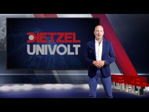 Lehrlingsportal.at Ein Mann in einem blauen Anzug steht in einem Studio neben einem Bildschirm mit der Aufschrift "Dietzel Univolt".