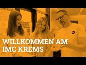 Lehrlingsportal.at Drei Personen stehen gemeinsam in einem Raum und betrachten einen durchsichtigen Behälter; darüber ist der Text „WILLKOMMEN AM IMC KREMS“ zu lesen.