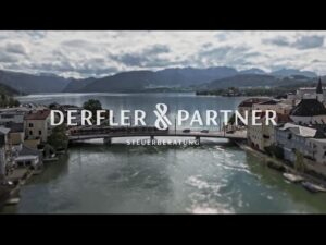 Lehrlingsportal.at Ein Fluss fließt durch eine Stadt mit einer Brücke und Gebäuden auf beiden Seiten, Berge im Hintergrund; der Text lautet "Derfler & Partner Steuerberatung".