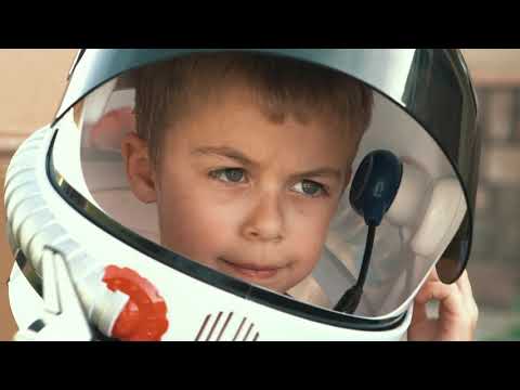 Lehrlingsportal.at Ein kleiner Junge trägt einen Spielzeug-Astronautenhelm und schaut aufmerksam durch das Visier, wobei ein Teil des Helms im Vordergrund zu sehen ist.