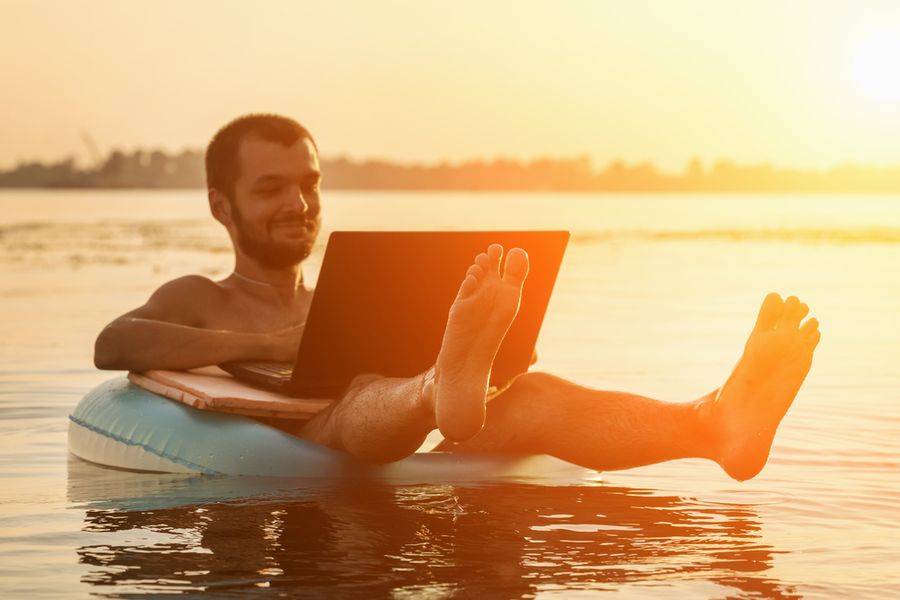 Lehrlingsportal.at Ein Mann treibt in einem Gummiring auf einem See und arbeitet an einem Laptop. Im Hintergrund ist der Sonnenuntergang zu sehen.