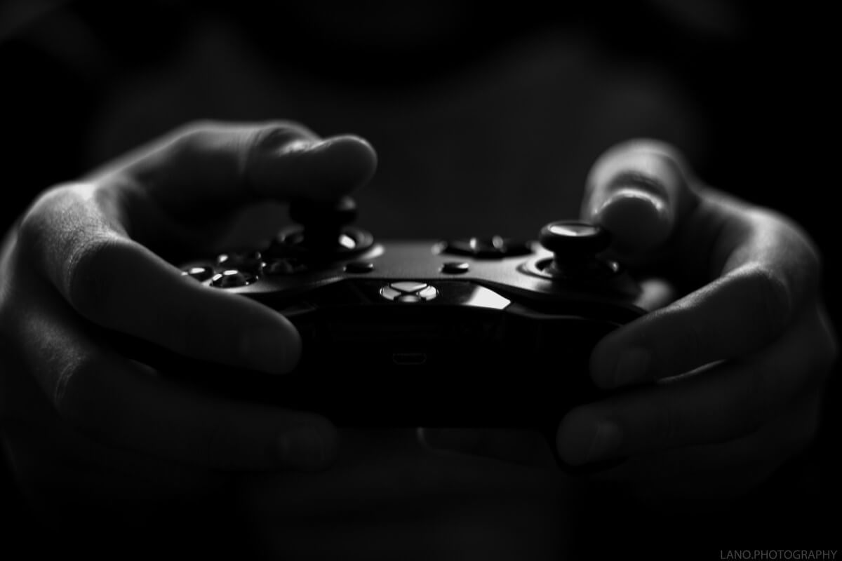 Lehrlingsportal.at Nahaufnahme von Händen, die in einer dunklen Umgebung einen Videospiel-Controller halten.