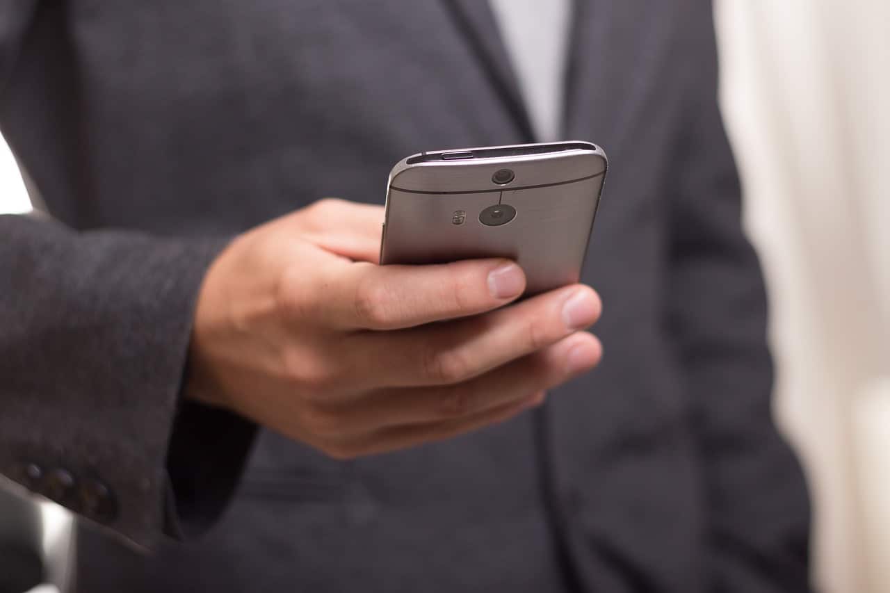 Lehrlingsportal.at Eine Person im Anzug hält ein Smartphone in der Hand.