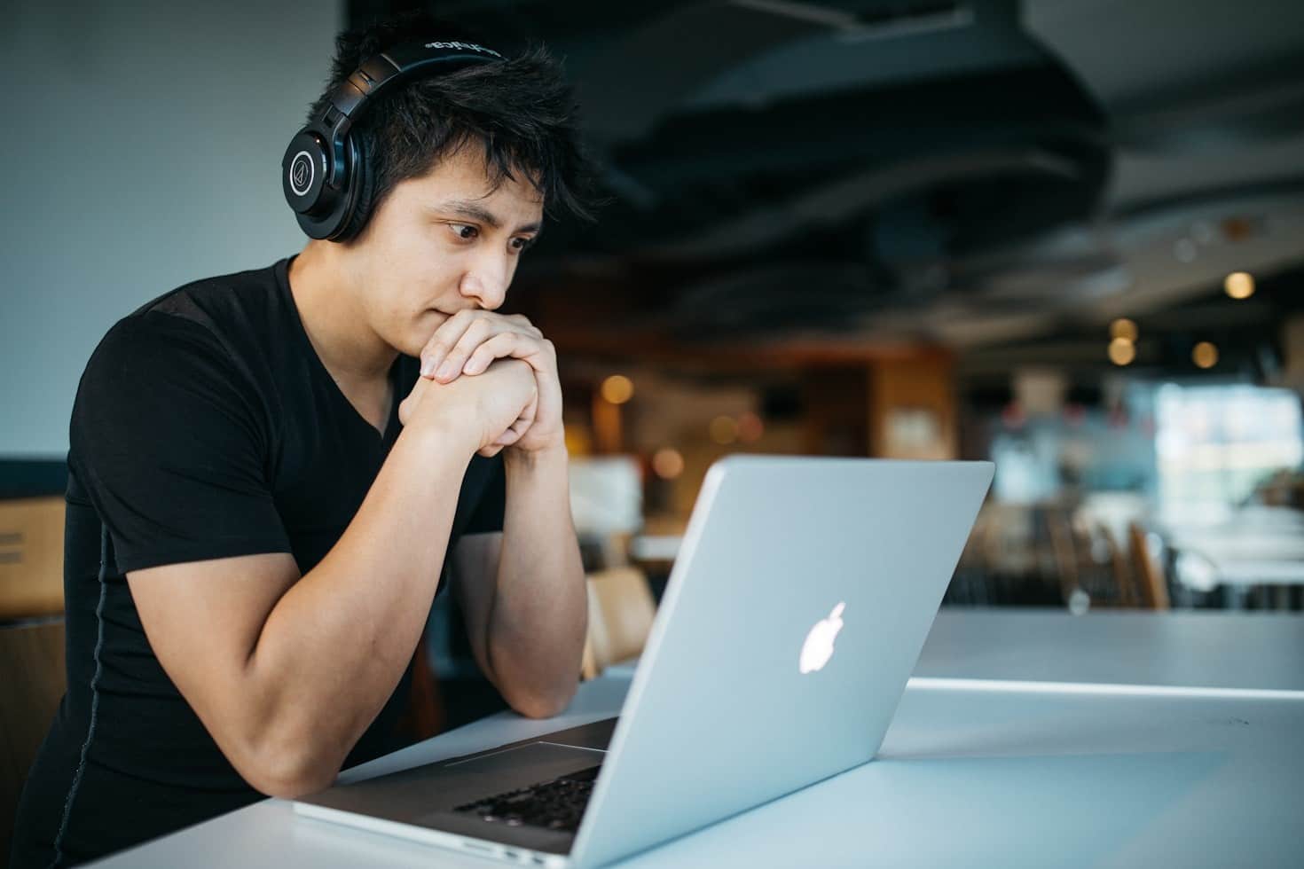 Lehrlingsportal.at Eine Person mit Kopfhörern sitzt an einem Tisch und blickt aufmerksam auf einen Laptop-Bildschirm in einer modernen Innenumgebung.
