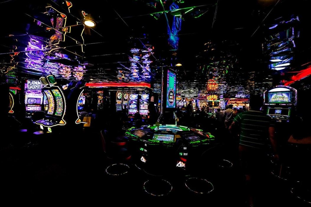 Lehrlingsportal.at Ein schwach beleuchtetes Casino voller Spielautomaten und bunter Neonlichter.