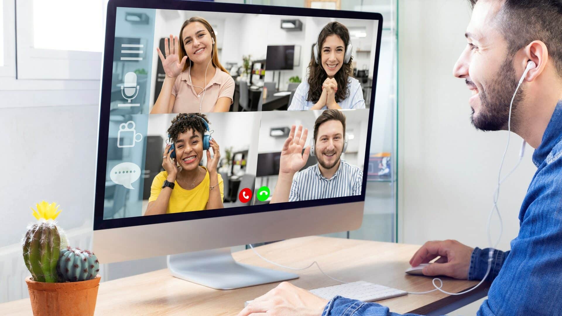 Lehrlingsportal.at Ein Mann nimmt an einem Videoanruf mit vier Personen auf einem Computerbildschirm teil, jede Person winkt und lächelt, mit einem Kaktus auf dem Schreibtisch.