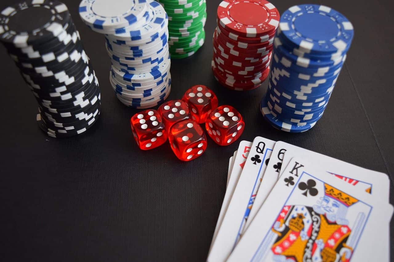 Lehrlingsportal.at Pokerchips in verschiedenen Farben, rote Würfel und ein Kartenspiel mit drei Königen und zwei Damen auf schwarzem Untergrund.