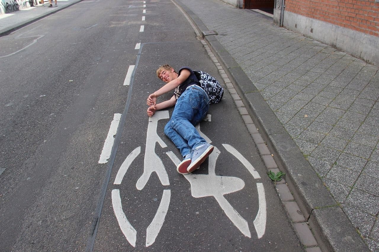 Lehrlingsportal.at Auf einem Radweg liegende Person, die die Position eines Fahrradsymbols auf dem Bürgersteig nachahmt.