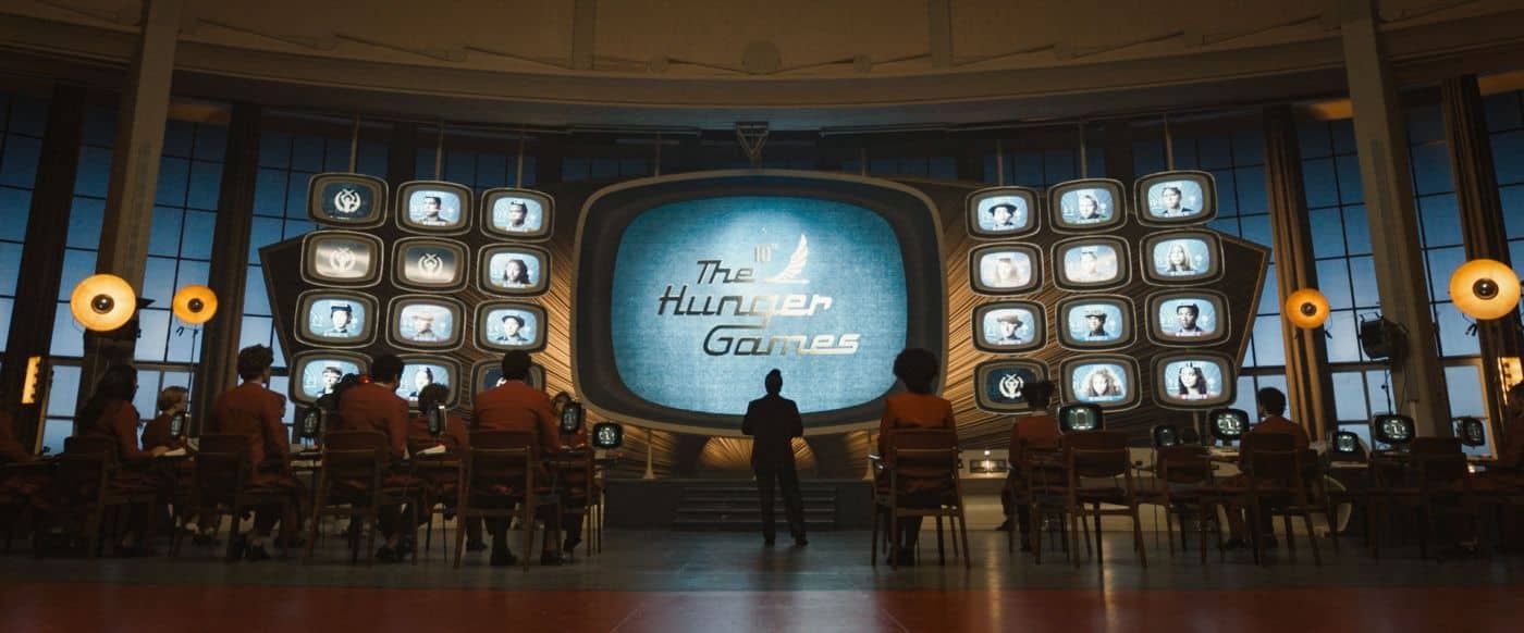 Lehrlingsportal.at In einem großen Kontrollraum im Retro-Stil werden mehrere Bildschirme angezeigt, auf dem zentralen Monitor läuft "Die Tribute von Panem". Die Leute sitzen an Konsolen und blicken auf die Bildschirme.