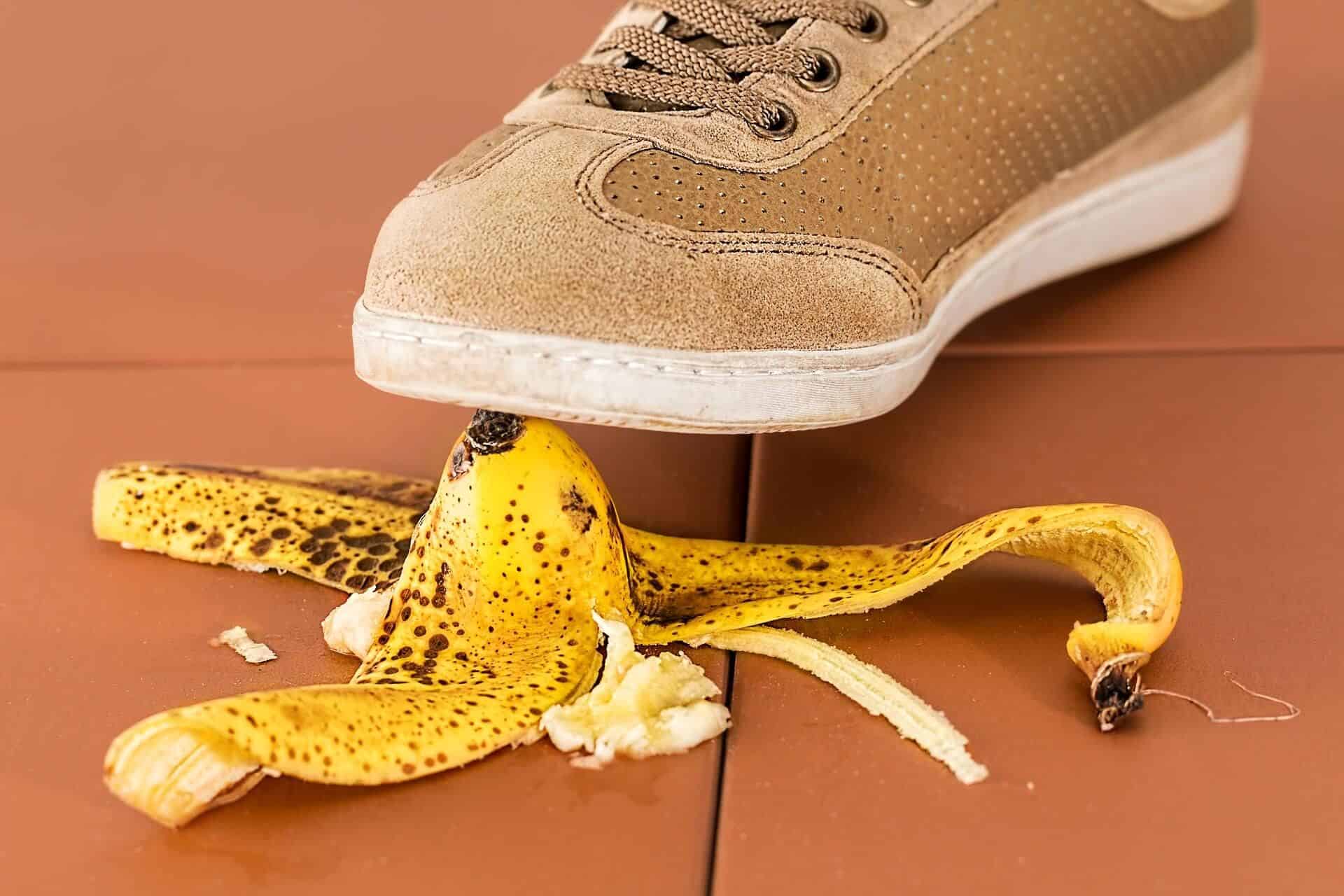 Lehrlingsportal.at Ein Turnschuh, der im Begriff ist, auf eine Bananenschale auf einem gefliesten Boden zu treten.
