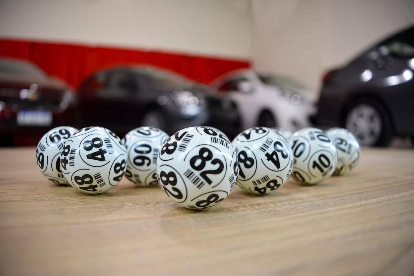 Lehrlingsportal.at Bingokugeln mit den Zahlen 48, 69, 88, 90 usw. liegen auf einer Holzoberfläche. Im unscharfen Hintergrund sind Autos geparkt.