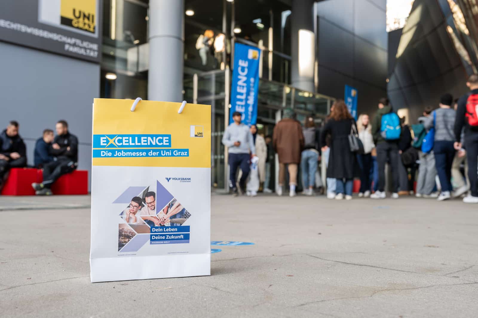 Lehrlingsportal.at Vor einem Gebäude ist eine Werbetasche für die Jobmesse der Universität Graz zu sehen; davor hat sich eine Gruppe von Menschen versammelt, die in einer Schlange stehen.