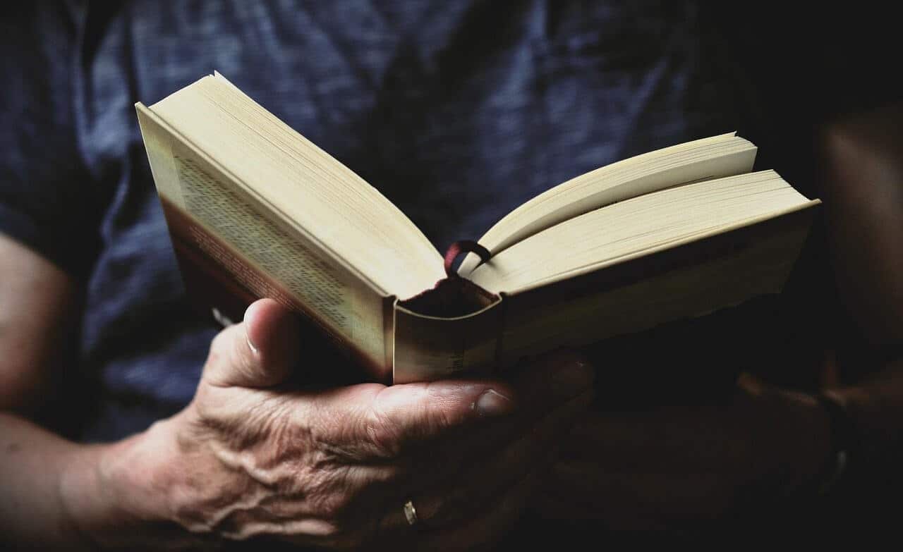 Lehrlingsportal.at Nahaufnahme einer Person in einem dunklen Hemd, die ein offenes Buch hält und liest, wobei ein Lesebändchen sichtbar ist.