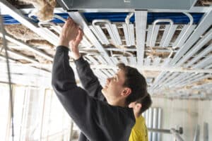 Lehrlingsportal.at Zwei Arbeiter installieren oder justieren elektrische Leitungen und Metallkonstruktionen an einer im Bau befindlichen Gebäudedecke.
