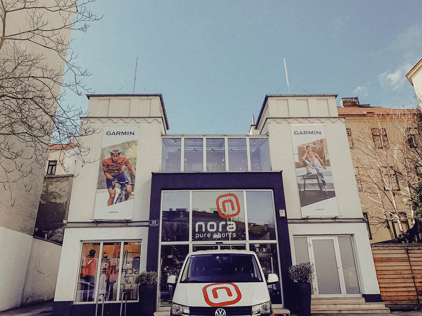 Lehrlingsportal.at Ein Schaufenster mit der Aufschrift nora pure sports", große Radfahrer-Plakate auf jeder Seite und ein weißer Lieferwagen, der davor geparkt ist.