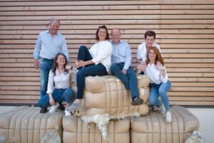 Lehrlingsportal.at Fünf Personen posieren lächelnd und in legerer blau-weißer Kleidung auf und um große Wollballen an einer Holzlattenwand.