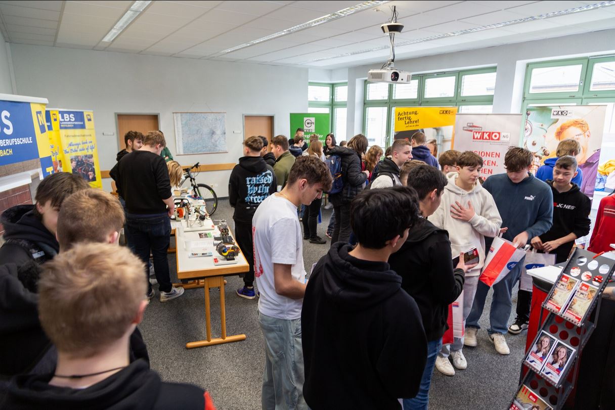 Lehrlingsportal.at Eine Gruppe von Schülern erkundet eine überdachte Karrieremesse und besucht Stände mit Informationsmaterial und Broschüren in einem Klassenzimmer.