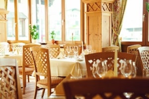 Lehrlingsportal.at Ein heller Restaurantbereich mit Holzstühlen, Tischen mit Glasgeschirr und großen Fenstern, die den Raum mit natürlichem Licht erfüllen.