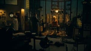 Lehrlingsportal.at Eine Frau sitzt auf einem Stuhl, umgeben von Kabeln in einem schwach beleuchteten Labor, während zwei Personen, eine davon in einem Laborkittel, in der Nähe zwischen wissenschaftlichen Geräten und Maschinen stehen.