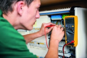 Lehrlingsportal.at Person, die mit einem Digitalmultimeter die Spannung in einer Schalttafel misst, wobei das Display einen Wert von 240,0 Volt anzeigt.