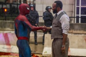Lehrlingsportal.at Eine Person in einem Spider-Man-Kostüm gibt einem Mann in Weste und Krawatte im Freien bei Regen die Hand, im Hintergrund sind Polizeibeamte und Absperrungen zu sehen.
