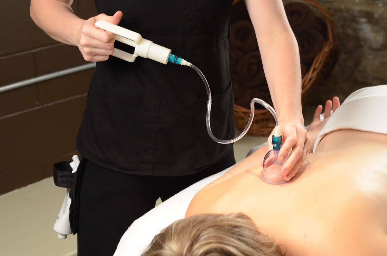 Lehrlingsportal.at Während einer Schröpftherapie-Sitzung bringt eine Person mit Hilfe eines handgeführten Absauggeräts einen Plastikbecher auf dem nackten Rücken einer anderen Person an.