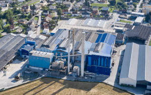 Lehrlingsportal.at Luftaufnahme einer großen Industrieanlage mit blauen Gebäuden, hohen Schornsteinen sowie umliegenden Wohnhäusern und Feldern.