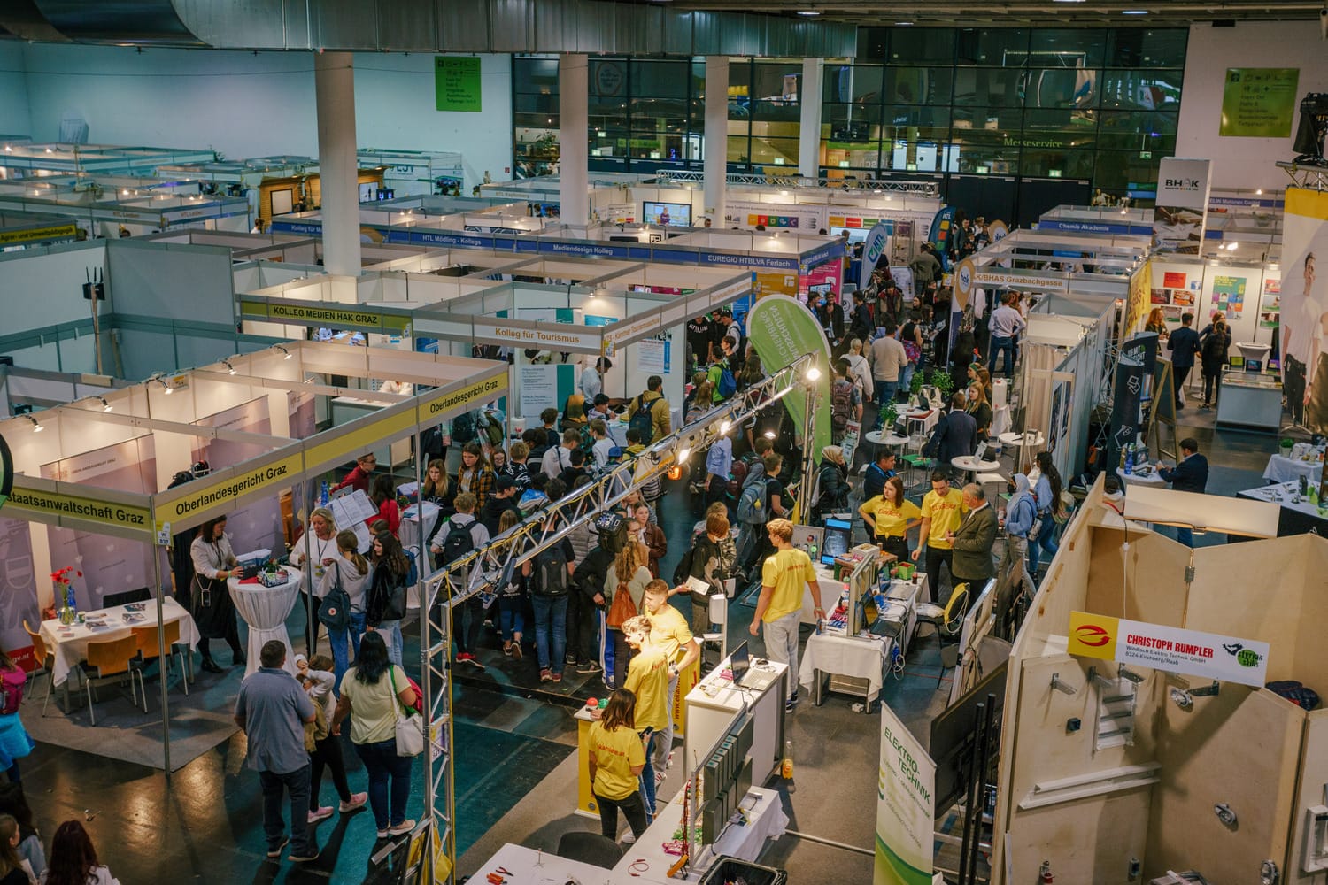 Lehrlingsportal.at Eine Menschenmenge schlendert zwischen den Ausstellungsständen einer Messe in einer Halle umher, in der überall Ausstellungsstücke, Banner und verschiedene Informationsstände zu sehen sind.
