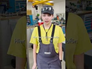 Lehrlingsportal.at Eine Person in einem gelben Hemd, einer grauen Latzhose, einer Mütze und einer Brille steht in einer Werkstatt. Auf dem Bildschirm erscheint ein Text auf Deutsch.