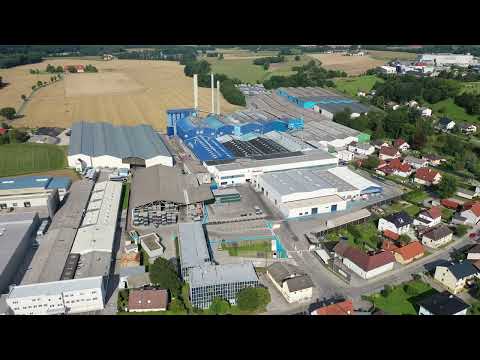 Lehrlingsportal.at Luftaufnahme eines Industriekomplexes mit blau-weißen Gebäuden neben Wohnhäusern und Feldern.