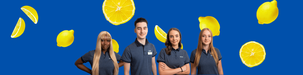 Lehrlingsportal.at Vier Mitarbeiter in einheitlichen grauen Poloshirts stehen vor einem blauen Hintergrund mit schwebenden Zitronen.