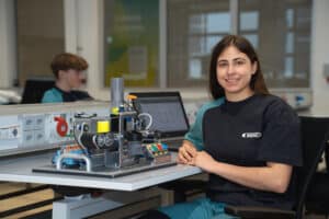 Lehrlingsportal.at Ein Student in einem Buhler-Shirt sitzt an einem Schreibtisch mit einem Schulungsmodul zur Industrieautomation.