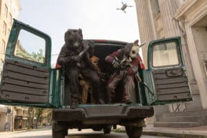 Lehrlingsportal.at Zwei Gestalten mit Tiermasken und Gewehren sitzen hinten in einem offenen Transporter, während über ihnen eine Drohne fliegt.