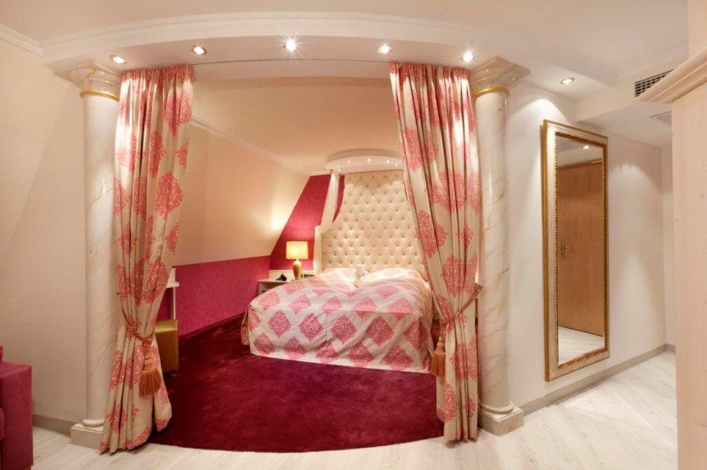 Hotelzimmer mit Doppelbett rotem Samtteppich und opulenten Vorhängen