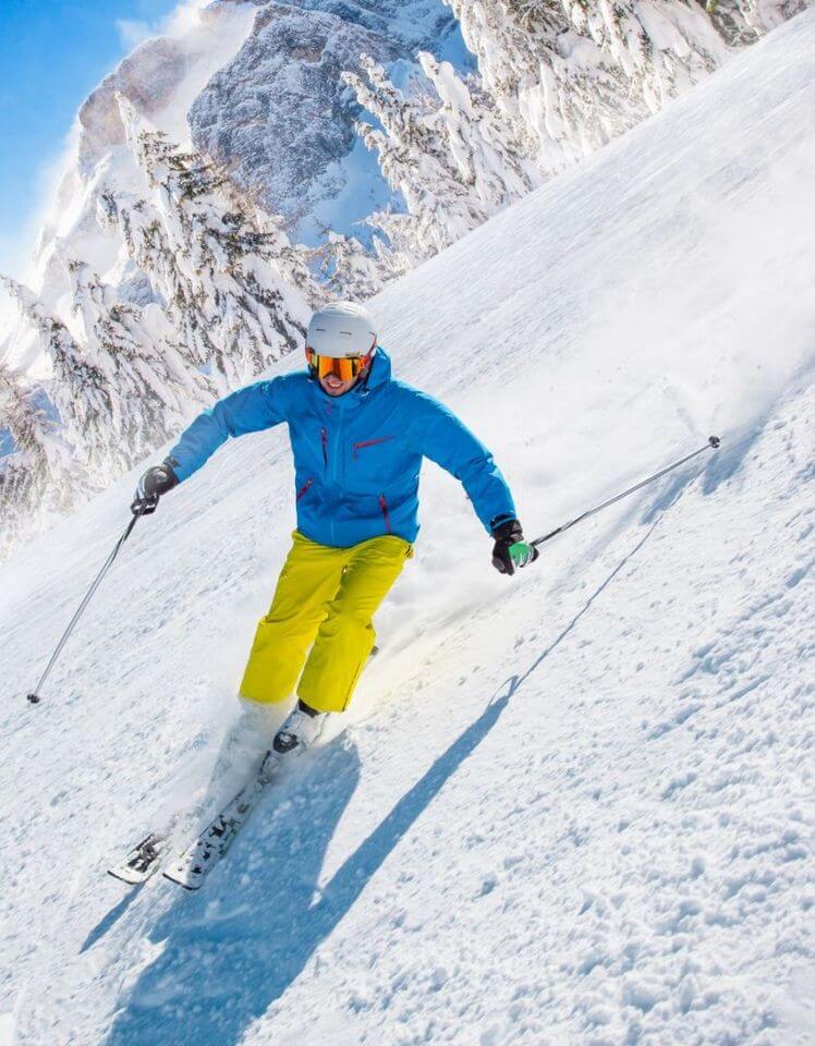 Skifahrer in gelber Skihose und blauer Jacke bei strahlendem Sonnenschein