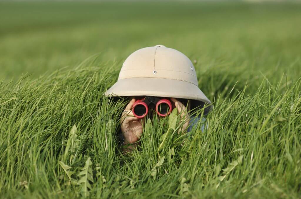 Kind mit Hut und Fernglas versteckt sich im Gras