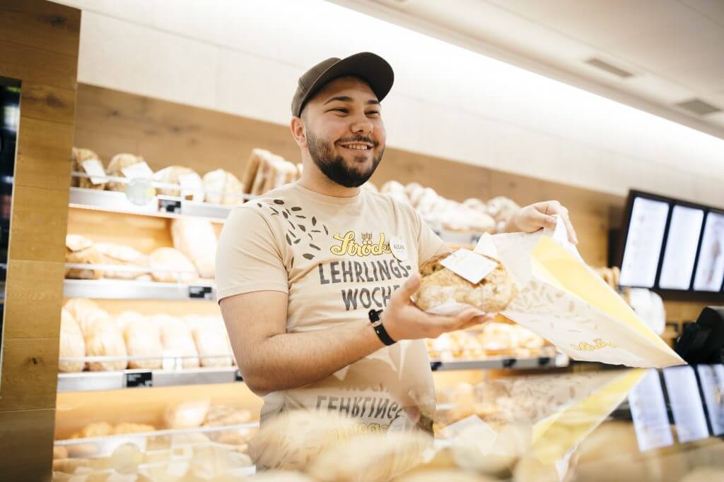 Lehrbetrieb Stroeck Junger Mann Mit Kappe Verpackt Brot In Shop