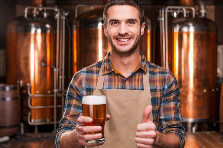 Mann mit Daumen hoch hält ein Glas Bier in der Hand