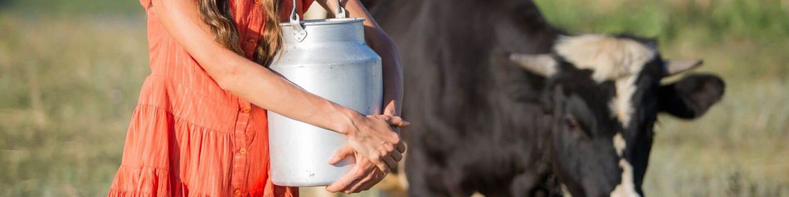 Bäuerin steht mit einer Milchkanne und ihrer Kuh auf der Weide