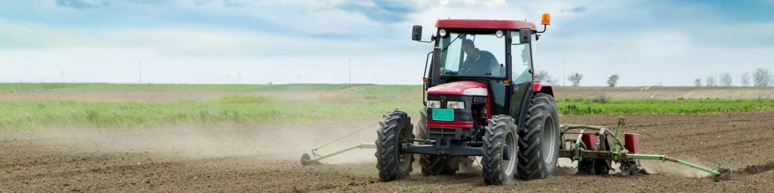 Ein Bauer sät mit seinem roten Traktor das Feld